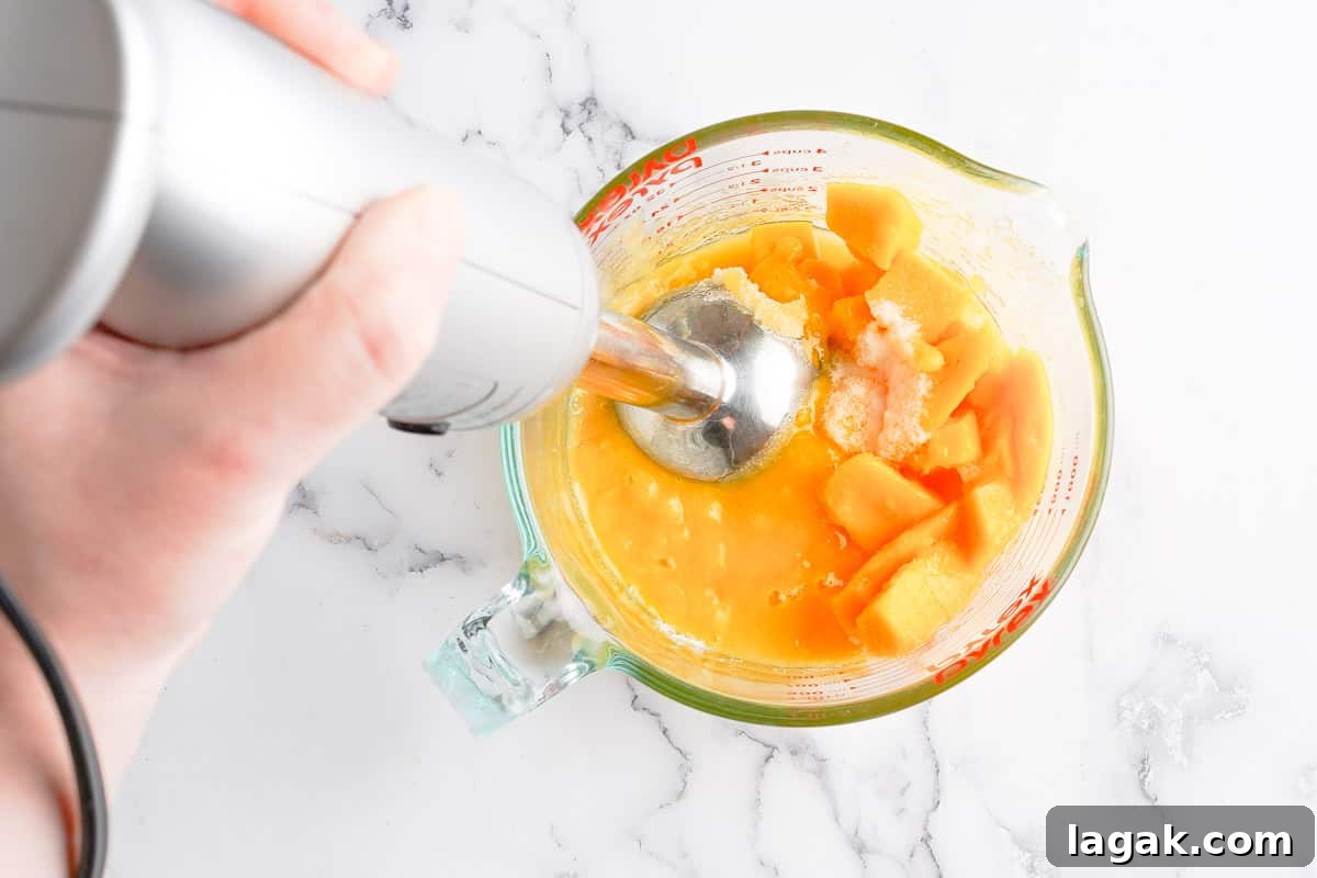 stick blender blending up popsicle ingredients in glass measuring cup