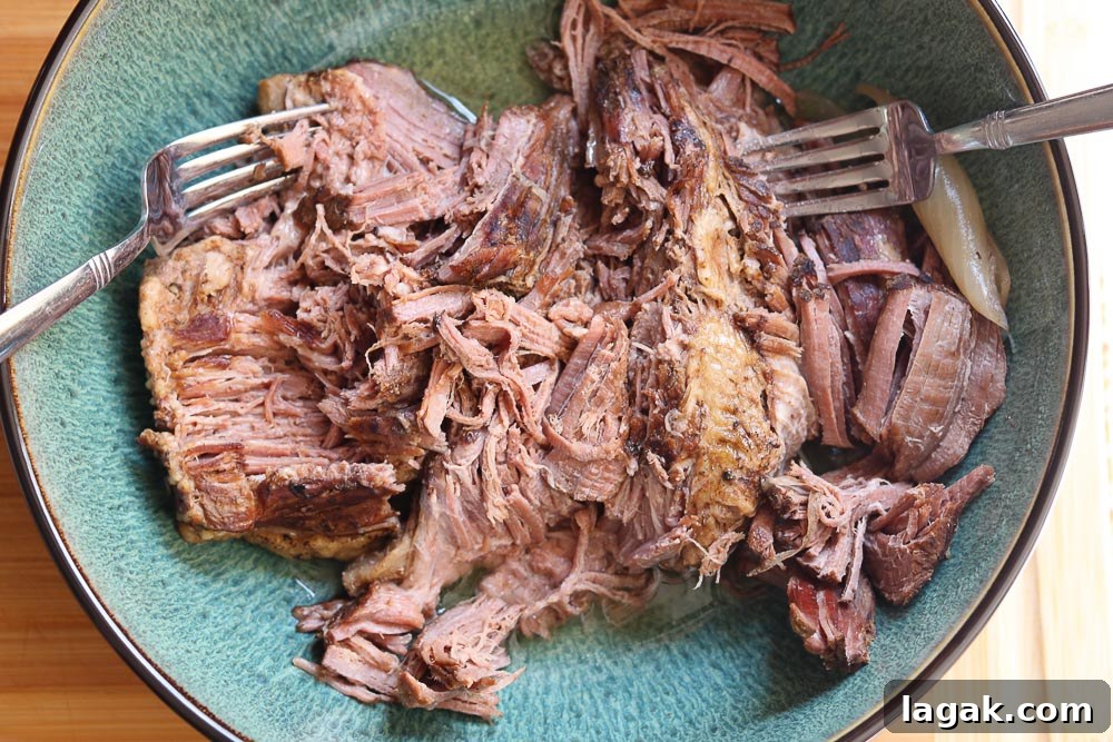 cooked brisket in bowl with forks for shredding 