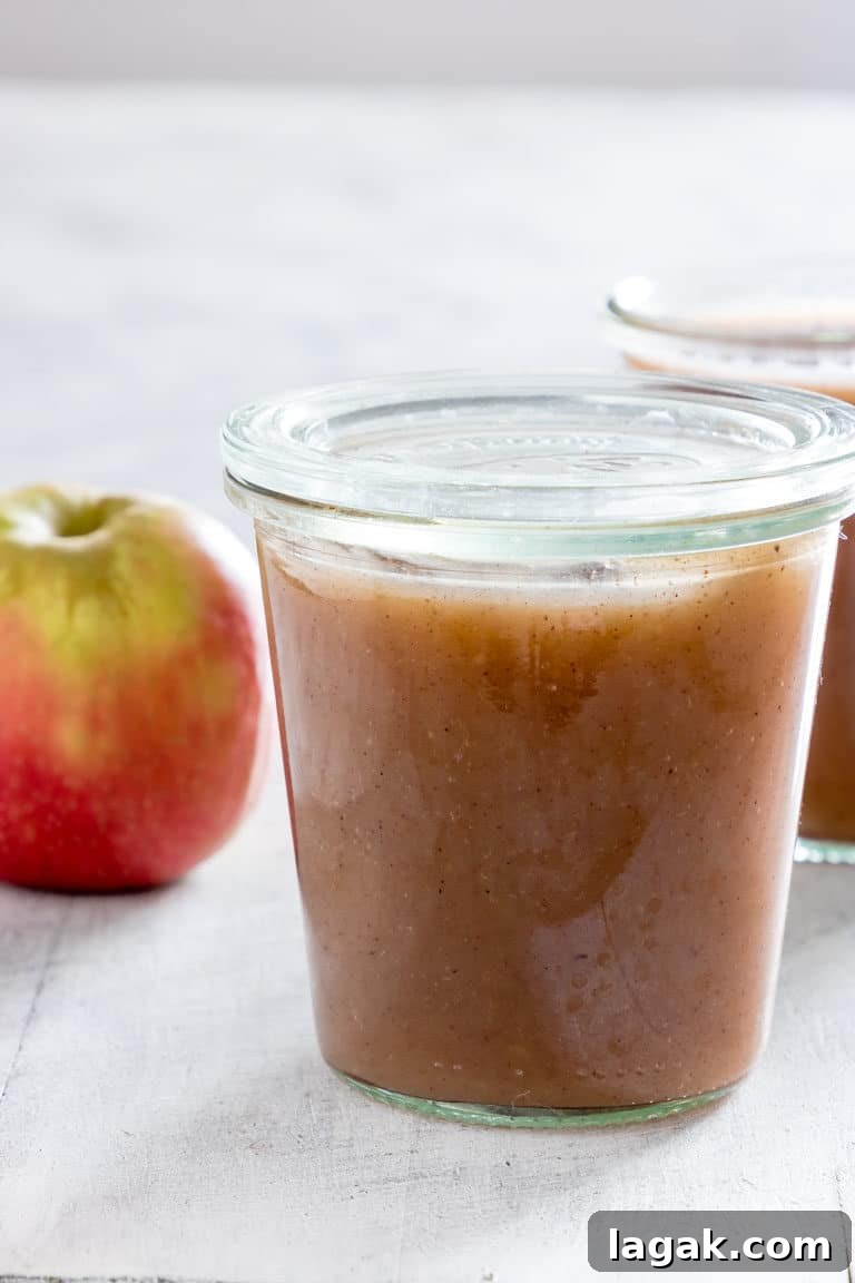 A jar full of Instant Pot Applesauce with apple and another jar in the background