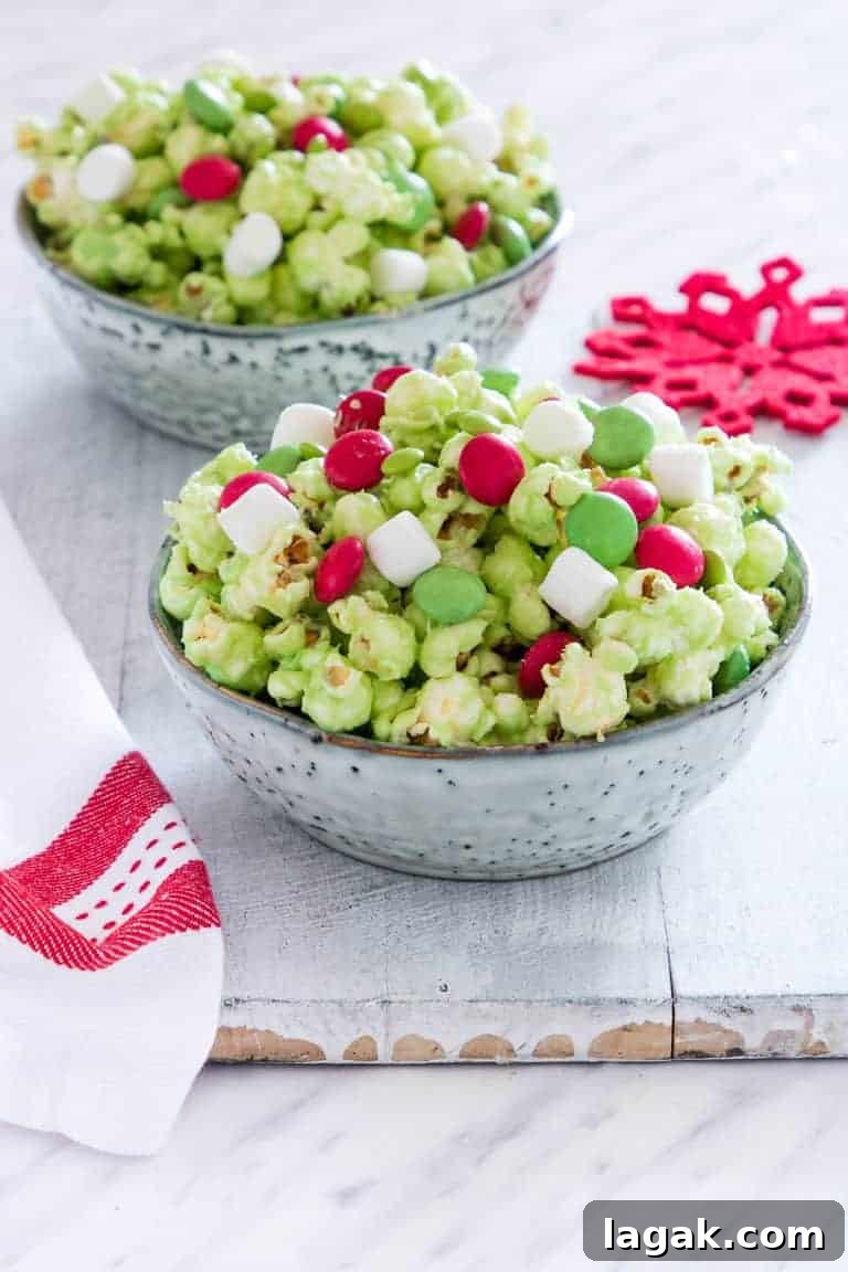 two ceramic bowls filled with Grinch Popcorn on a wooden table next to red print cloth napkin and festive red snowflake coaster
