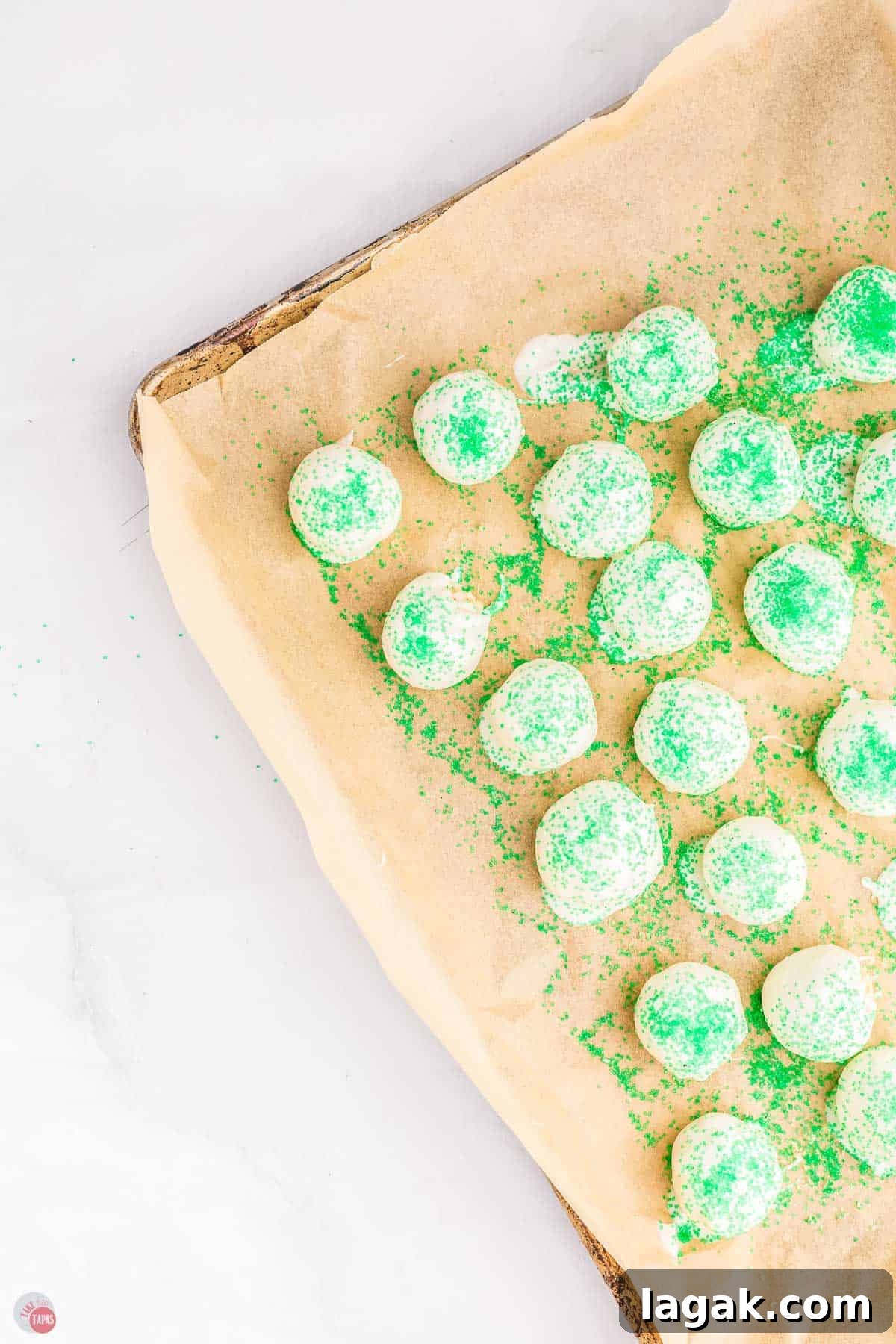 white cake balls on a baking sheet covered with green sprinkles