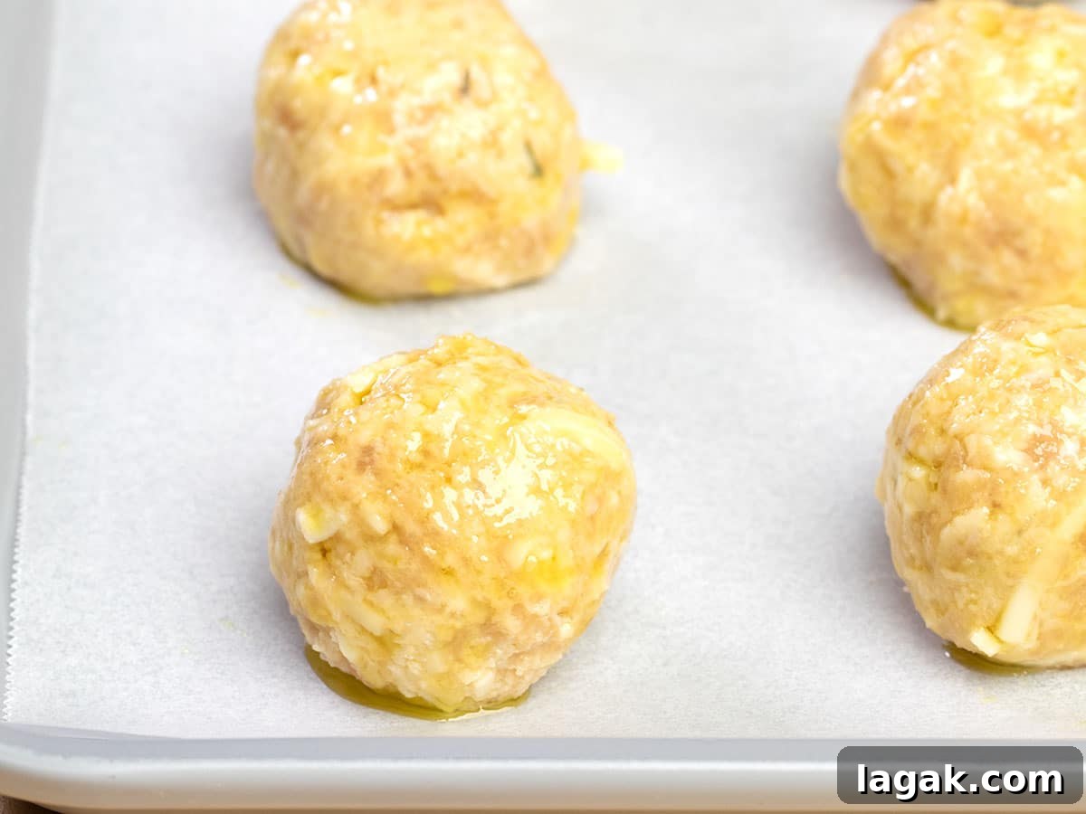 closeup image of 4 raw shaped baked chicken meatballs with olive oil on white paper