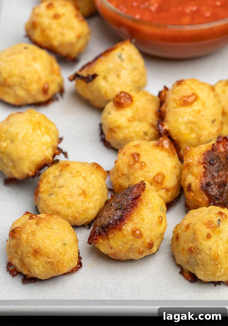 12 baked chicken meatballs on white paper on tray with small bowl of red tomato sauce