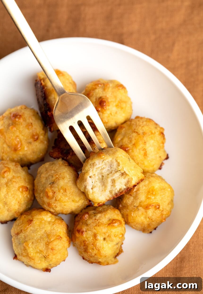 11 baked chicken meatballs in wide flat white bowl with gold fork with one meatball broken in half