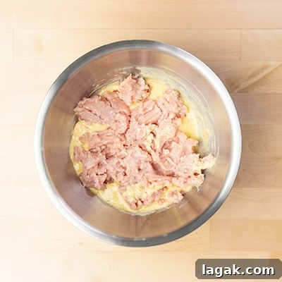 same mixing bowl with crumbled ground chicken on top of yellow liquid