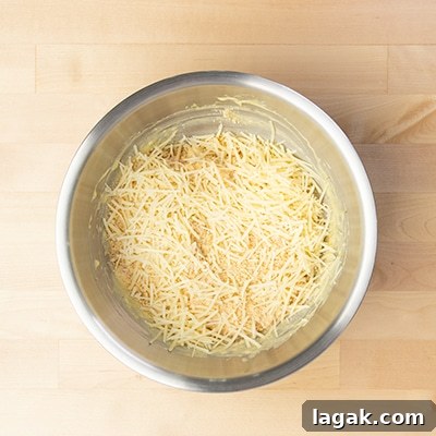 shredded parmesan cheese on top of chicken mixture in mixing bowl