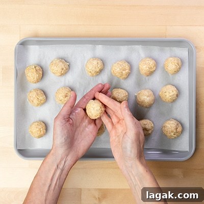 hands shaping raw chicken meatball mixture into rounds with fingers