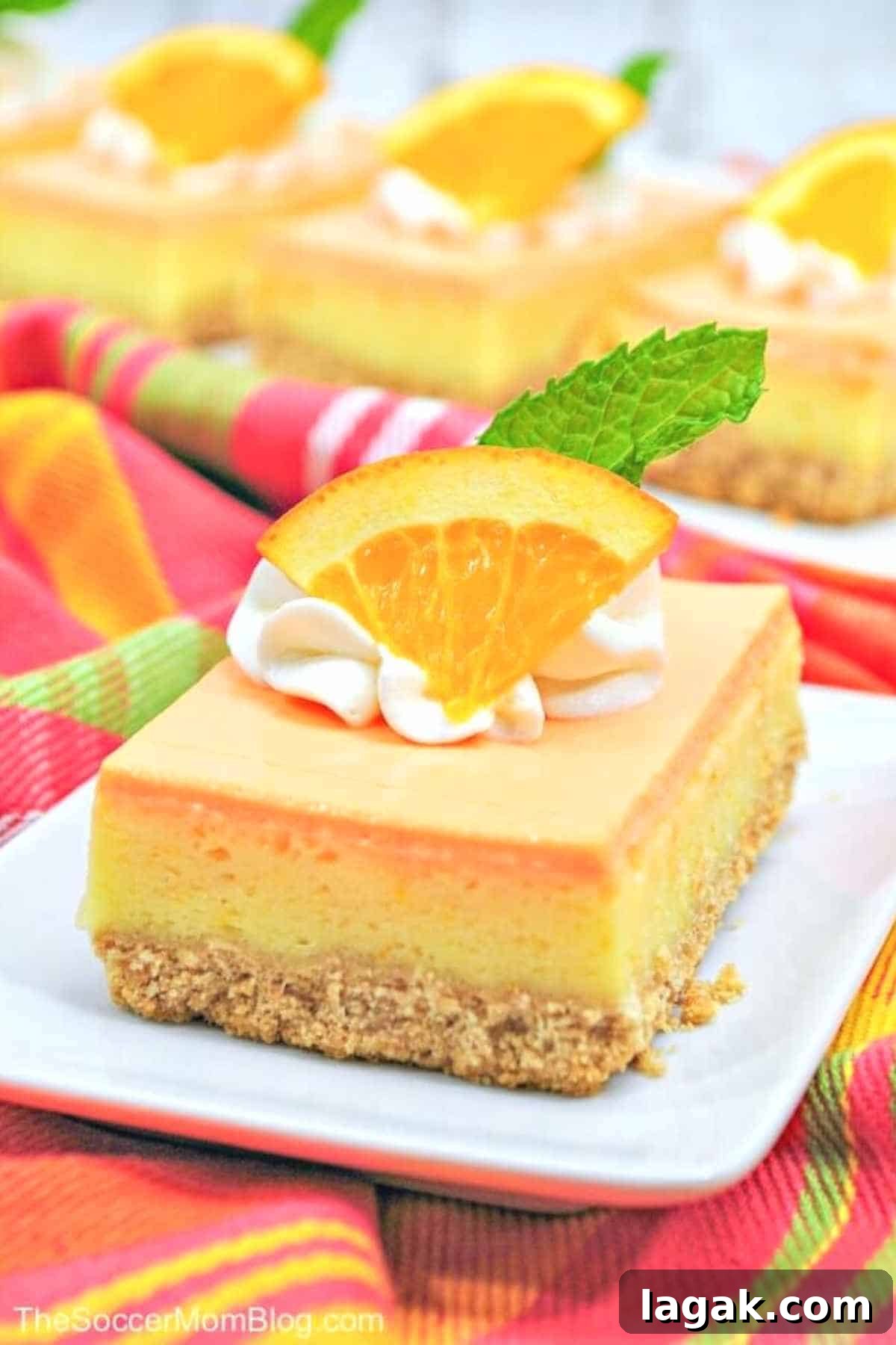 orange creamsicle cheesecake bars placed on a white plate with vibrant tea towel on the side