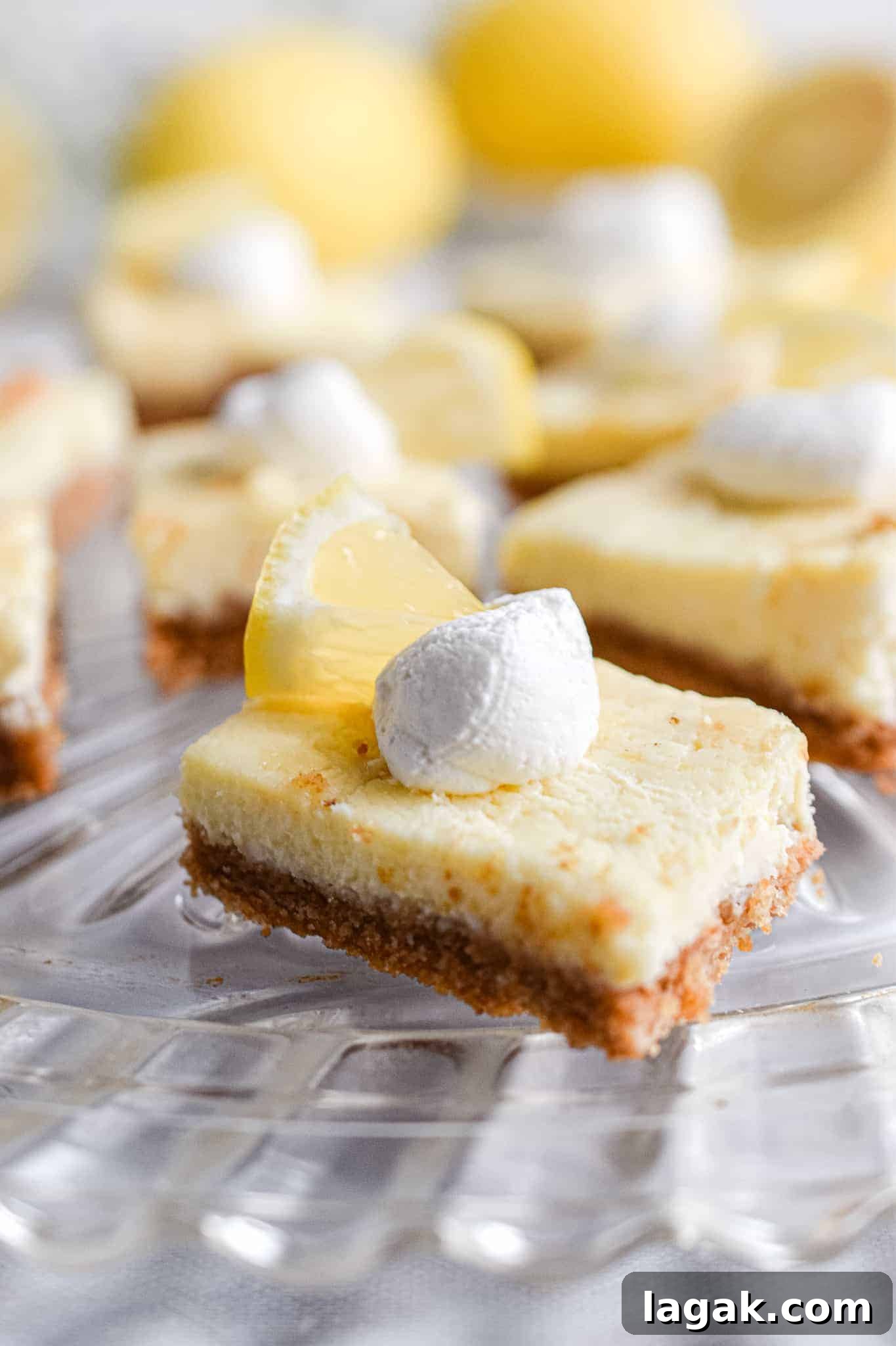 lemon cheesecake bars placed on glass plate with a dollop of cream and lemon wedge on top placed on